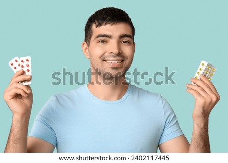 Young man with blisters of vitamin A pills on blue background, closeup