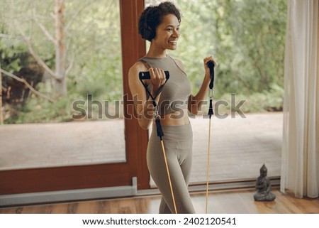 Close up of sporty woman in headphones exercising with a sports elastic band at home Royalty-Free Stock Photo #2402120541