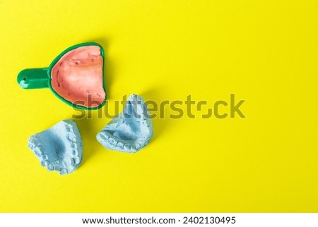 Blue plaster cast of a dental jaw and a dental tray for an impression of a dental jaw on a yellow background. The concept of orthodontics in dentistry, the manufacture of dentures and crowns.  Royalty-Free Stock Photo #2402130495
