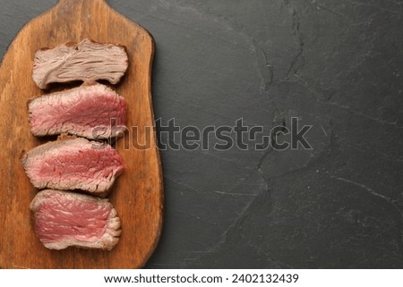Delicious sliced beef tenderloin with different degrees of doneness on black table, top view. Space for text Royalty-Free Stock Photo #2402132439