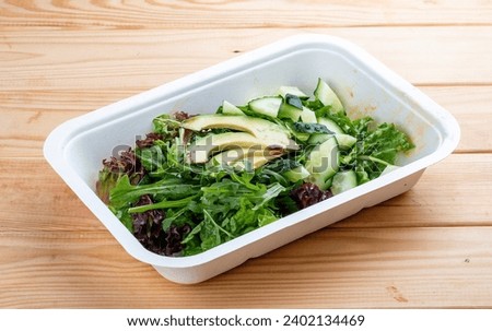 Salad with greens and avocado. Vegetarian food. Takeaway food. On a wooden background.