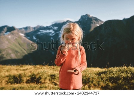 Child girl eating cookies snacks in mountains adventure travel family vacations outdoor active healthy lifestyle 4 years old kid blonde hair exploring Norway 