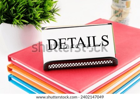 DETAILS text on a white business card standing on a stand on notebooks, next to the money out of focus and a green plant on a white background