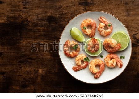 Shrimps, overhead flat lay shot with copy space. Fried shrimp with lime on a white plate, shot from the top on a rustic wooden background. Keto appetizer Royalty-Free Stock Photo #2402148263