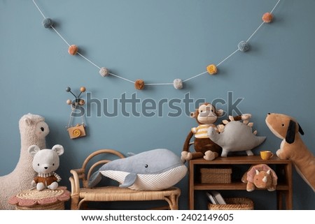 Aesthetic composition of warm child room interior with wooden sideboard, blue wall, stylish armchair, garland on wall, plush monkey, toys, wooden camera and personal accessories. Home decor. Template.