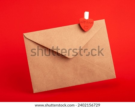 Envelope made of kraft paper with clothespin heart on red background.