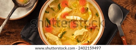 Chicken noodle soup with vegetables panorama, a bowl of healthy broth, overhead flat lay shot on a rustic wooden table, panoramic banner