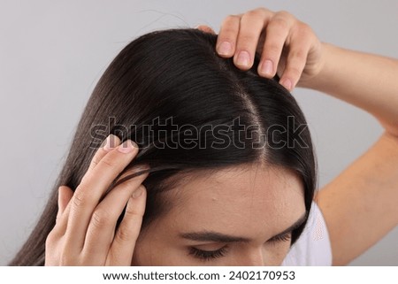 Woman examining her hair and scalp on grey background, closeup Royalty-Free Stock Photo #2402170953