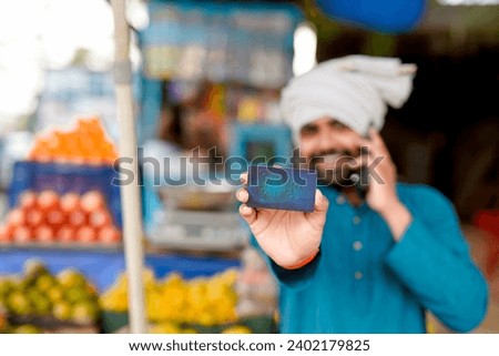 Young Indian fruit seller showing debit or credit card and phone at the camera, mixing tradition with technology.