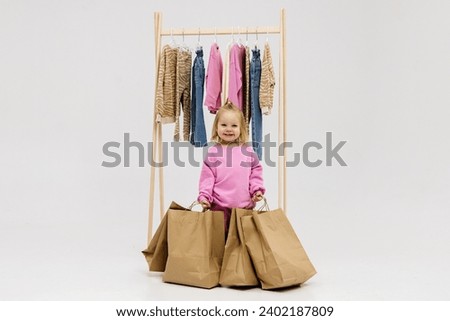 A child, a little girl, stands near the closet, chooses clothes against a light background. Dressing room with clothes on hangers. Wardrobe of children's and stylish clothes. Montessori wardrobe. Royalty-Free Stock Photo #2402187809