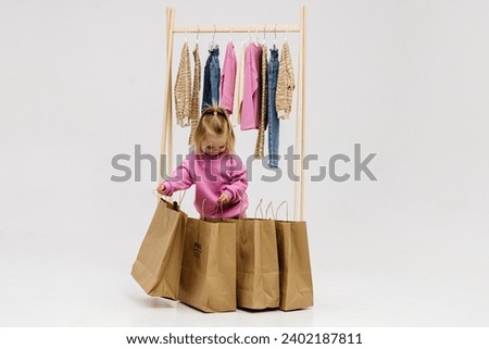 A child, a little girl, stands near the closet, chooses clothes against a light background. Dressing room with clothes on hangers. Wardrobe of children's and stylish clothes. Montessori wardrobe. Royalty-Free Stock Photo #2402187811