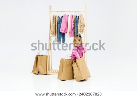 A child, a little girl, stands near the closet, chooses clothes against a light background. Dressing room with clothes on hangers. Wardrobe of children's and stylish clothes. Montessori wardrobe. Royalty-Free Stock Photo #2402187823