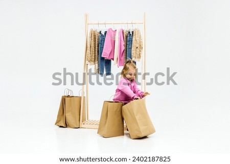 A child, a little girl, stands near the closet, chooses clothes against a light background. Dressing room with clothes on hangers. Wardrobe of children's and stylish clothes. Montessori wardrobe. Royalty-Free Stock Photo #2402187825