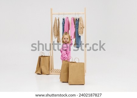 A child, a little girl, stands near the closet, chooses clothes against a light background. Dressing room with clothes on hangers. Wardrobe of children's and stylish clothes. Montessori wardrobe. Royalty-Free Stock Photo #2402187827