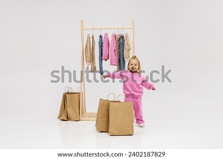 A child, a little girl, stands near the closet, chooses clothes against a light background. Dressing room with clothes on hangers. Wardrobe of children's and stylish clothes. Montessori wardrobe. Royalty-Free Stock Photo #2402187829