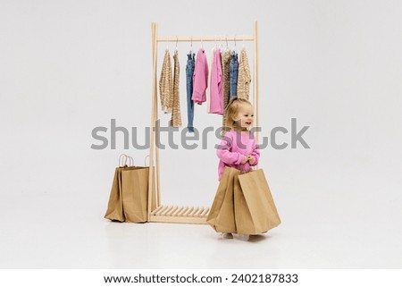 A child, a little girl, stands near the closet, chooses clothes against a light background. Dressing room with clothes on hangers. Wardrobe of children's and stylish clothes. Montessori wardrobe. Royalty-Free Stock Photo #2402187833