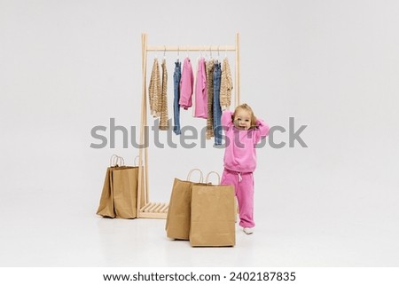 A child, a little girl, stands near the closet, chooses clothes against a light background. Dressing room with clothes on hangers. Wardrobe of children's and stylish clothes. Montessori wardrobe. Royalty-Free Stock Photo #2402187835