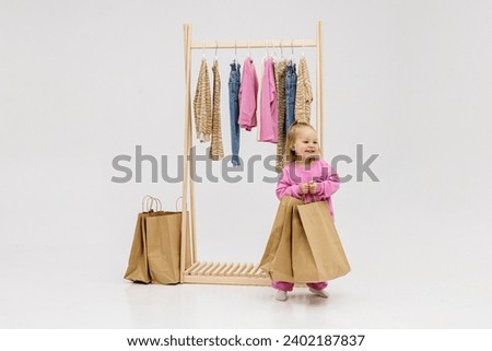 A child, a little girl, stands near the closet, chooses clothes against a light background. Dressing room with clothes on hangers. Wardrobe of children's and stylish clothes. Montessori wardrobe. Royalty-Free Stock Photo #2402187837