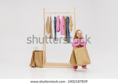 A child, a little girl, stands near the closet, chooses clothes against a light background. Dressing room with clothes on hangers. Wardrobe of children's and stylish clothes. Montessori wardrobe. Royalty-Free Stock Photo #2402187839