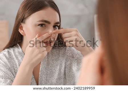 Young woman with skin problem looking at mirror indoors Royalty-Free Stock Photo #2402189959