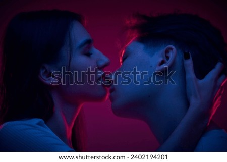 Tender young woman kissing her boyfriend, showing love and care against purple background in neon light. Concept of romance, love, relationship, passion, youth, dating, happiness