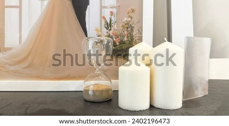 Big candles are beside the sand clock on a dusty dark table
