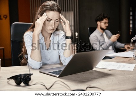 Young exhausted businesswoman feeling headache during working on laptop Royalty-Free Stock Photo #2402200779