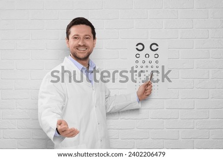 Ophthalmologist pointing at vision test chart on white brick wall Royalty-Free Stock Photo #2402206479