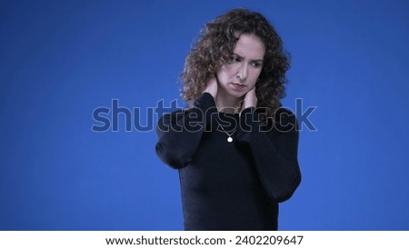 Stressed young woman rubbing neck trying to appease mental anguish while standing on blue background Royalty-Free Stock Photo #2402209647
