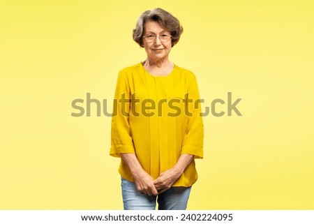 Beautiful smiling senior woman wearing eyeglasses and casual yellow blouse, looking at camera standing isolated on yellow background. Retired concept Royalty-Free Stock Photo #2402224095