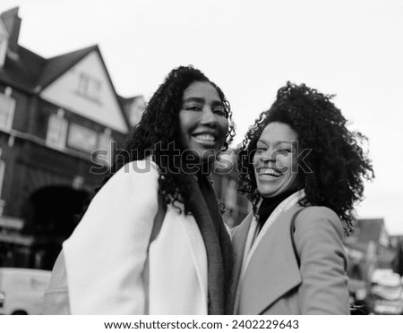 Analog film image of two carefree female friends in the street looking at camera and laughing. It is a monochromatic portrait made by a medium format old camera.