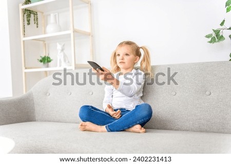 A Blond girl holding remote control on sofa at home