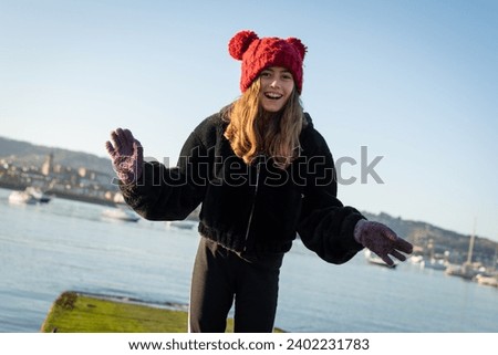 Smiling girl with a winter coat, hat and gloves in front of the Txingudi Bay, on the border between Spain and France, with the sea in the background, during a clear and sunny winter day