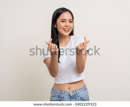 Pretty Young beautiful Asian woman standing and smiling showing mini heart sign on isolated white background. Attractive Lovely Latin female wearing white shirt feeling surprised and happy.