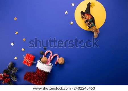 Epiphany day tradition. Befana and red stocking with sweet coal and candy on dark blue background.  Royalty-Free Stock Photo #2402245453