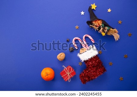 Epiphany day tradition. Befana and red stocking with sweet coal and candy on dark blue background.  Royalty-Free Stock Photo #2402245455