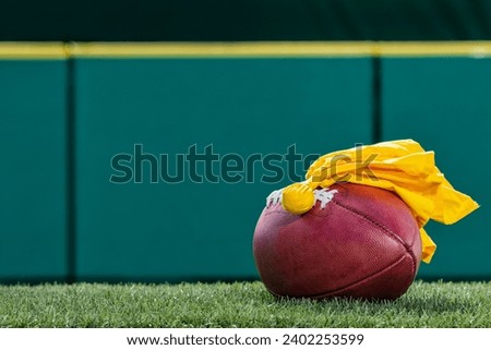 An American football with a yellow penalty flag sitting on top Royalty-Free Stock Photo #2402253599
