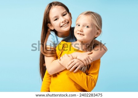 Portrait of smiling girls, cute sisters looking at camera isolated on blue background. Young happy fashion models posing for pictures in studio. Childhood, positive lifestyle concept 