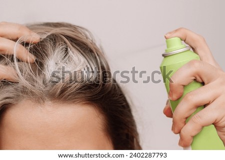 Close up of a young woman's head with dirty greasy hair. The girl spraying dry shampoo on the roots of her hair on a light background. The problem of oily scalp. A quick way to cleanse Royalty-Free Stock Photo #2402287793