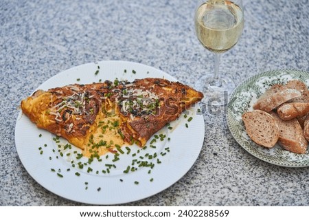 Close up picture on simple french style egg omelette with cheese and choped fresh chives served with slices of whole grain baguette and glass of white wine as a small and quick lunch in french bistro.