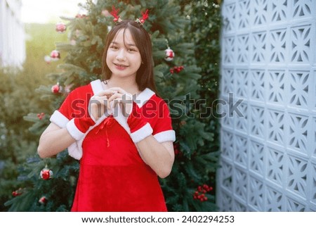 Portrait Cute Smiling asian girl in red santa with looking to the camera near Christmas greeting picture parcel decoration on Christmas tree background Decoration During Christmas and New Year.