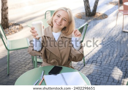 Food and drink concept. Young happy woman sitting in cafe, enjoying bright day outdoors, raising cup of coffee and smiling, drinking chai.