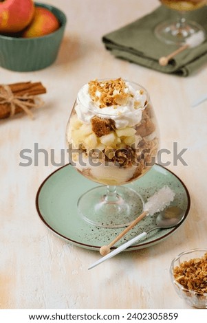 Dessert, portioned apple trifle with oat crumble, spiced cake, custard and whipped cream in a glass goblet on a light concrete background. Apple desserts, portioned desserts in glasses Royalty-Free Stock Photo #2402305859