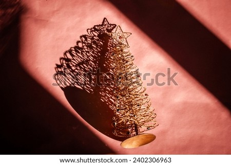 Decorative Christmas tree with a golden star on a top on pink table casts shadow. New Year 2024. Festive congratulation. Winter holidays, 31 December.