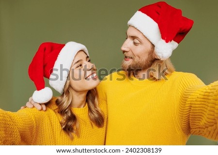 Close up merry young couple two friends man woman wear sweater Santa hat posing do selfie shot pov on mobile cell phone hug isolated on plain green background. Happy New Year Christmas holiday concept