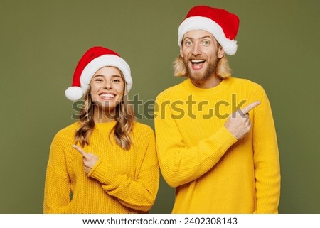 Merry surprised smiling young couple two friends man woman wear sweater Santa hat posing point index finger aside on area isolated on plain green background. Happy New Year Christmas holiday concept