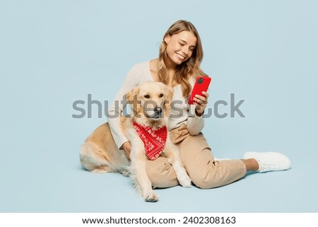 Full body happy young owner woman wear casual clothes sit with her best friend retriever dog in scarf use mobile cell phone isolated on plain light blue background studio. Take care about pet concept Royalty-Free Stock Photo #2402308163