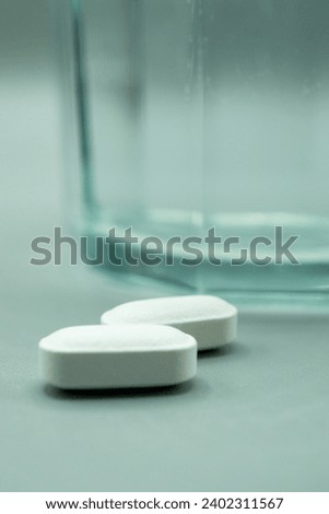 Pills next to glass of water on gray background