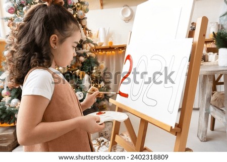 Talented schoolgirl artist paints red numbers 2024 on easel with palette and brush. Christmas tree background. Art school. Happy New Year Eve concept.