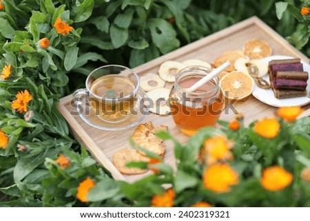 golden honey in a jar with a wooden spoon on a wooden tray among blooming calendula Fruit frips from orange persimmons pears and pasitila apples from raspberries and strawberries fresh tea with lemon 